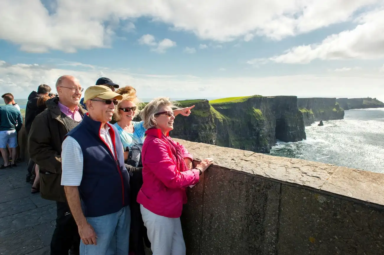 Enjoy ample free time to walk the scenic cliffside paths and feel the fresh ocean breeze. A group of happy tourists looking out over a stone wall at the spectacular Cliffs of Moher.