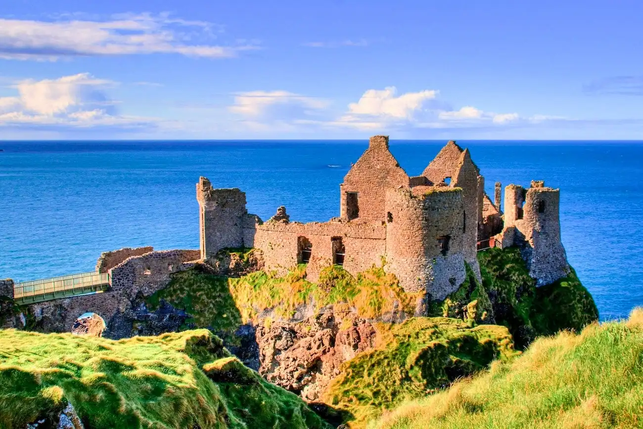 The dramatic ruins of Dunluce Castle perched precariously on a cliff edge overlooking the blue ocean.