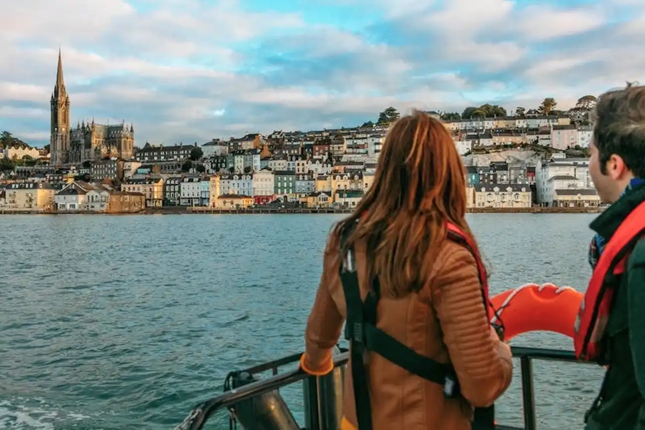 Two people looking at the colorful coastal town of Cóbh and St. Colman's Cathedral.