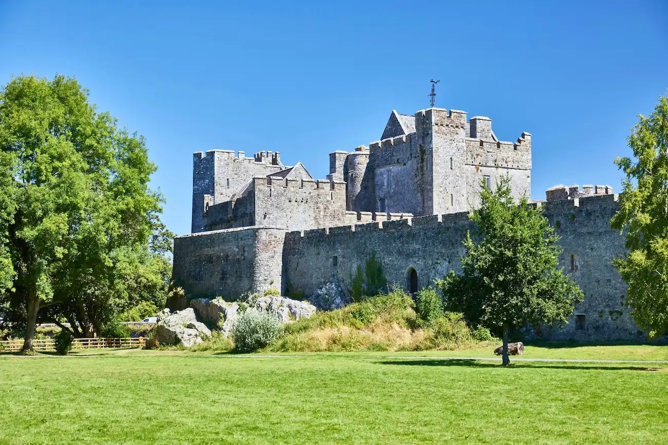 A wide view of the fortified stone walls of an ancient Irish castle on a sunny day.