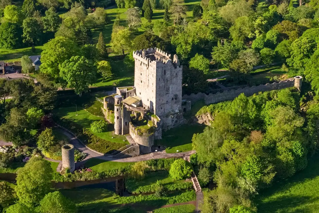 An aerial view of the famous Blarney Castle surrounded by dense, lush green forests and gardens.