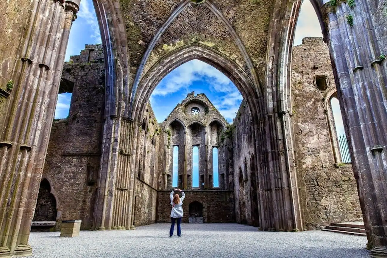 A tourist taking a photo inside the towering, roofless Gothic ruins of the Rock of Cashel.
