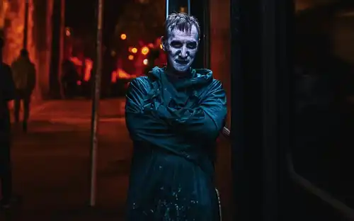A spooky actor in dark costume leaning against the Gravediggers Ghost Bus at night in Dublin.