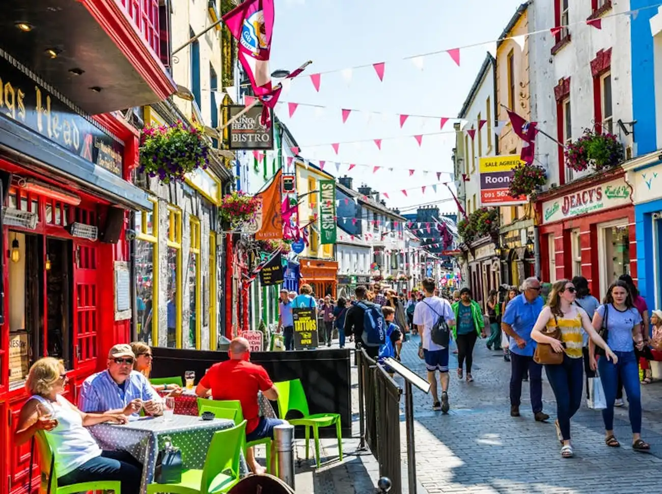 Spend an hour exploring the colorful streets, vibrant pubs, and lively buskers of bohemian Galway City. A lively, colorful pedestrian street in Galway City filled with traditional pubs, flags, and people.
