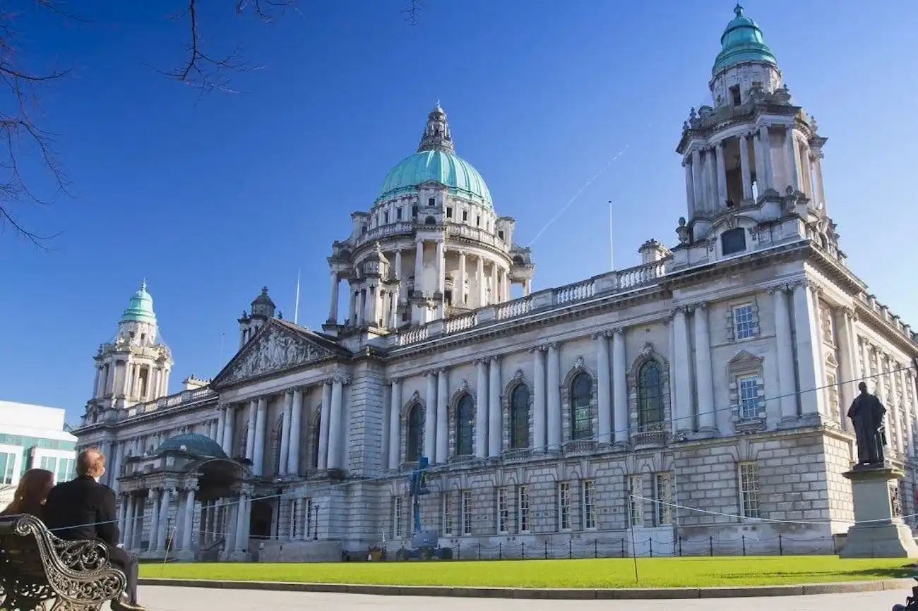 The impressive white stone architecture and green copper dome of Belfast City Hall against a blue sky.