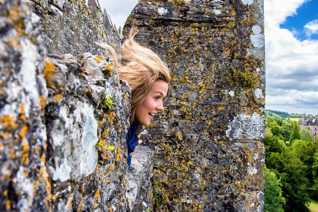 A woman leaning backwards over the castle battlements to kiss the legendary Blarney Stone.