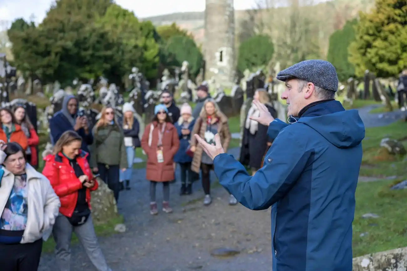 Join optional guided walking tours led by entertaining local experts to uncover local history. A professional tour guide in a blue jacket gesturing to an attentive group of travelers in front of an ancient stone tower.