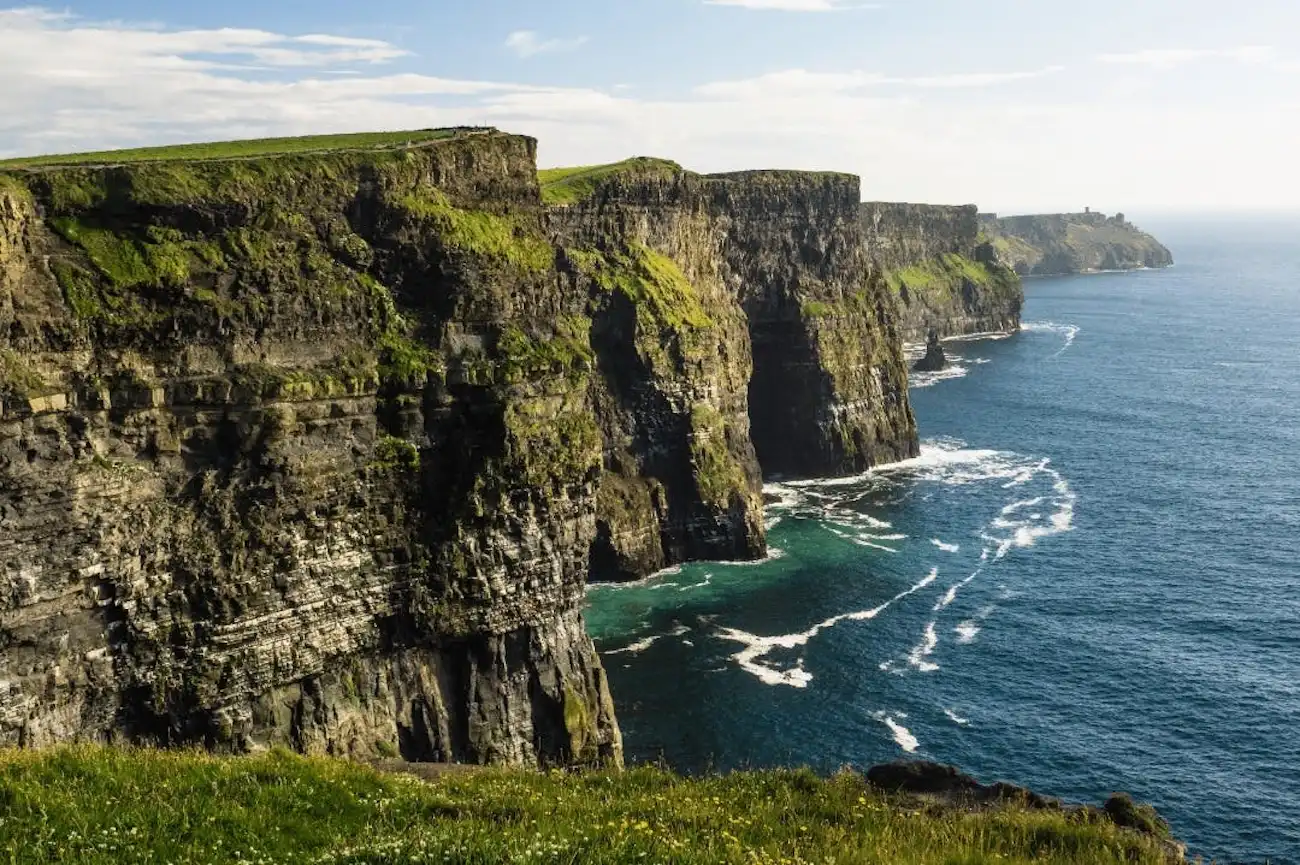 Marvel at the breathtaking, dramatic drops of the Cliffs of Moher on the Wild Atlantic Way. A breathtaking view along the rugged, green-topped edge of the Cliffs of Moher on a sunny day.