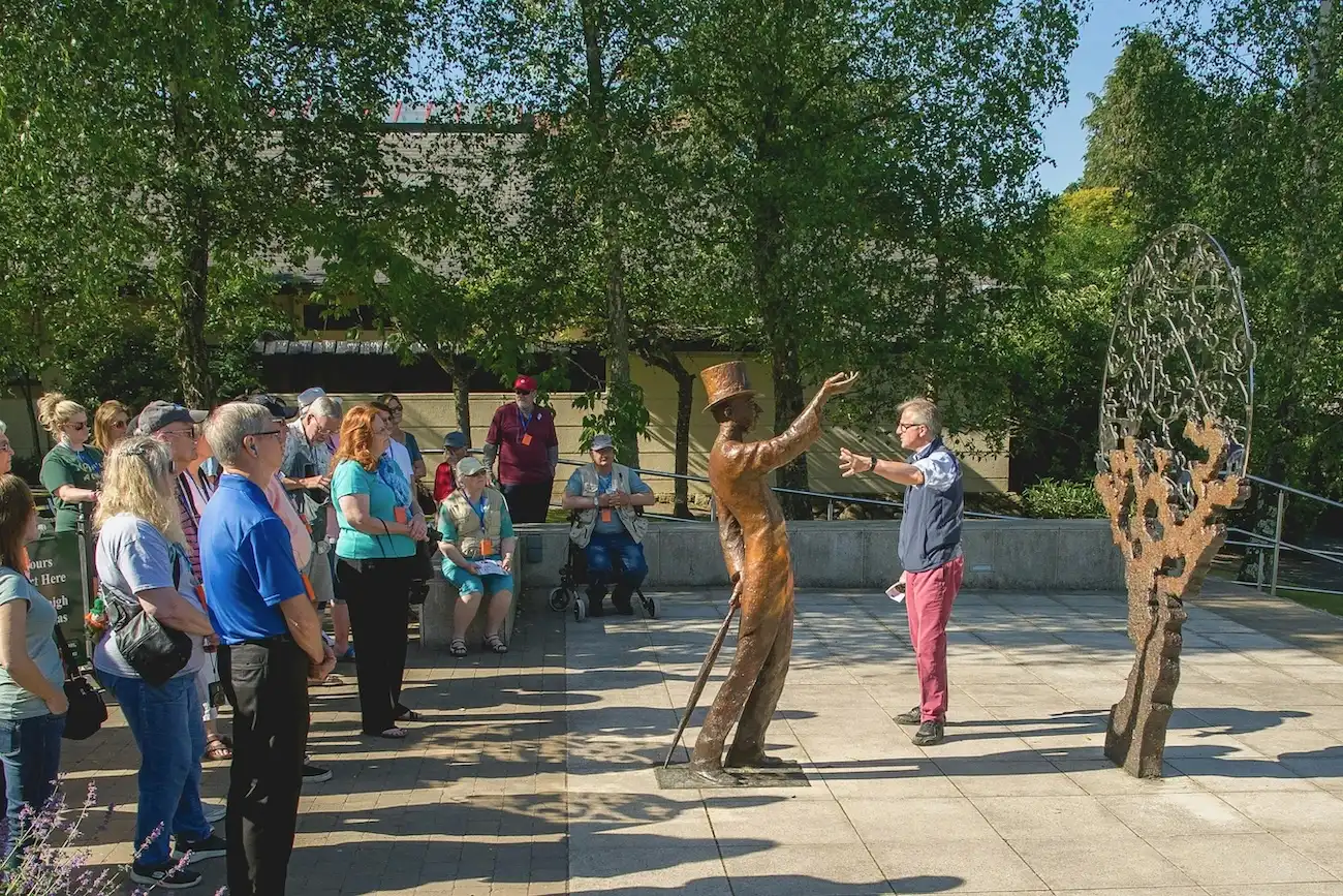 A tour guide speaking to a group of visitors near a bronze statue of a man at the Irish National Stud.